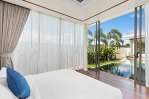 A bedroom with a large bed, a view of a swimming pool, and a glass door leading outside. - Bangtao Ozon Villas by My Home Phuket (Choeng Thale)