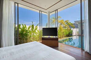 Ein modernes Hotelzimmer mit einem großen Bett, einem Fernseher und Blick auf einen Pool und Palmen.