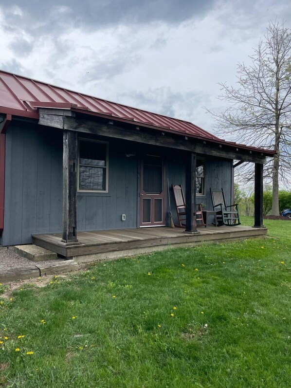 A rustic cabin with a red roof, a wooden porch, and a door with glass panels. - Charming Rustic Cottage in the Heart of Laurel Highlands, PA<br><br>Escape to this cozy, rustic retreat nestled in the stunning Laurel Highlands of Pennsylvania & Deer Creek Winery, where nature meets comfort & taste. Perfect for a weekend getaway or (Uniontown)