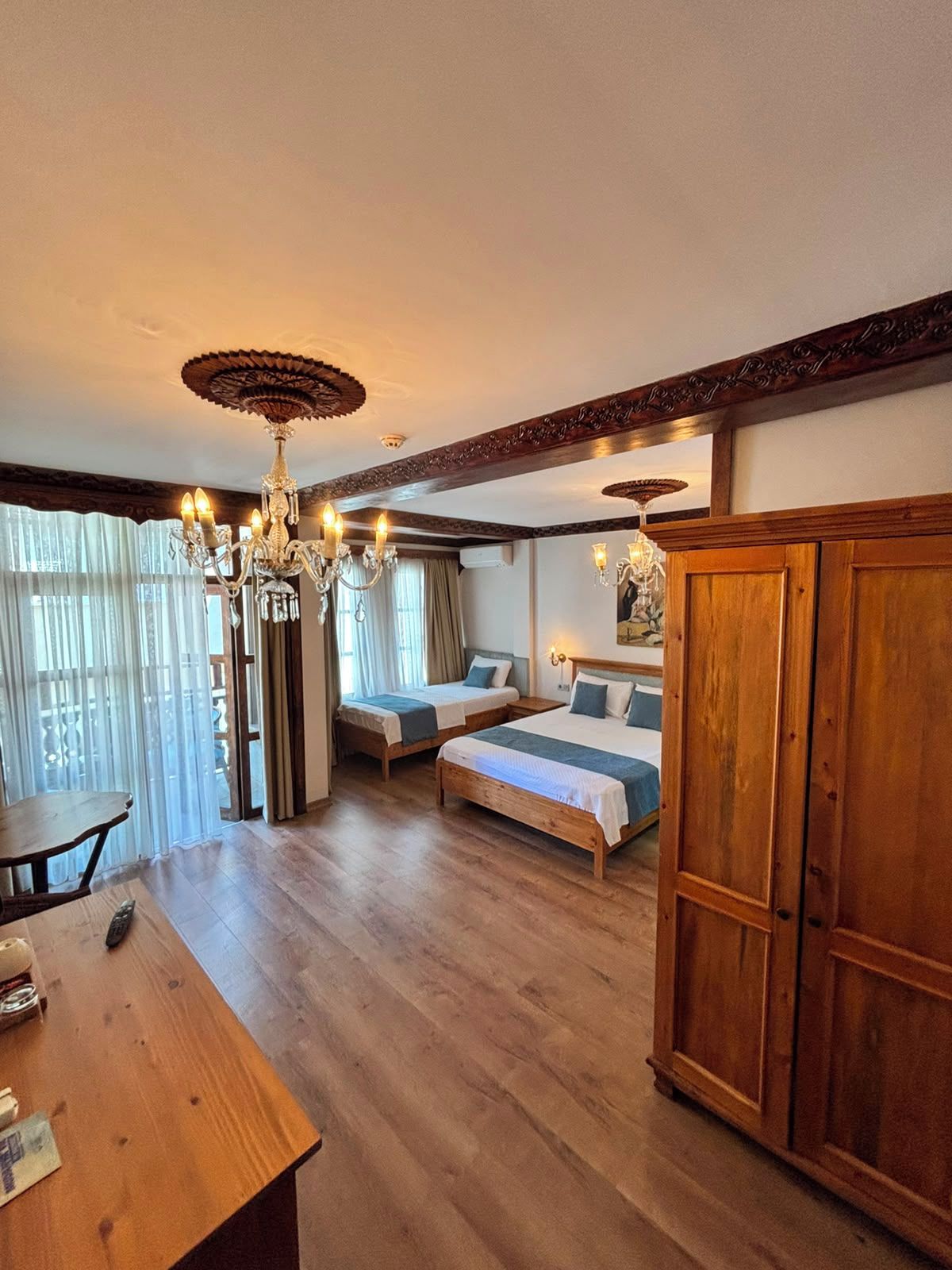 Habitación de hotel con dos camas, un armario de madera, una lámpara de araña y una mesa con un control remoto.
