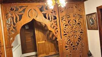 An ornate wooden doorway with intricate carvings, a chandelier, and a framed picture on the wall.