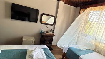 Habitación de hotel con dos camas, un televisor de pantalla plana, una mesita de noche con lámpara y una ventana con cortina translúcida.