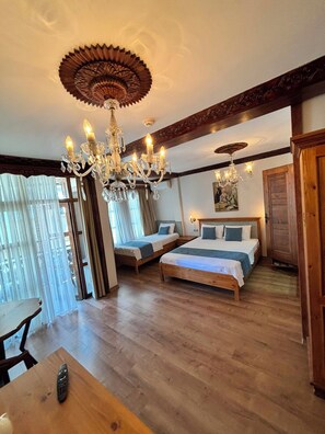 A hotel room with a chandelier, two beds, a wooden table, and a view through a window with sheer curtains. - DuruHanımKonağı (Mudanya)