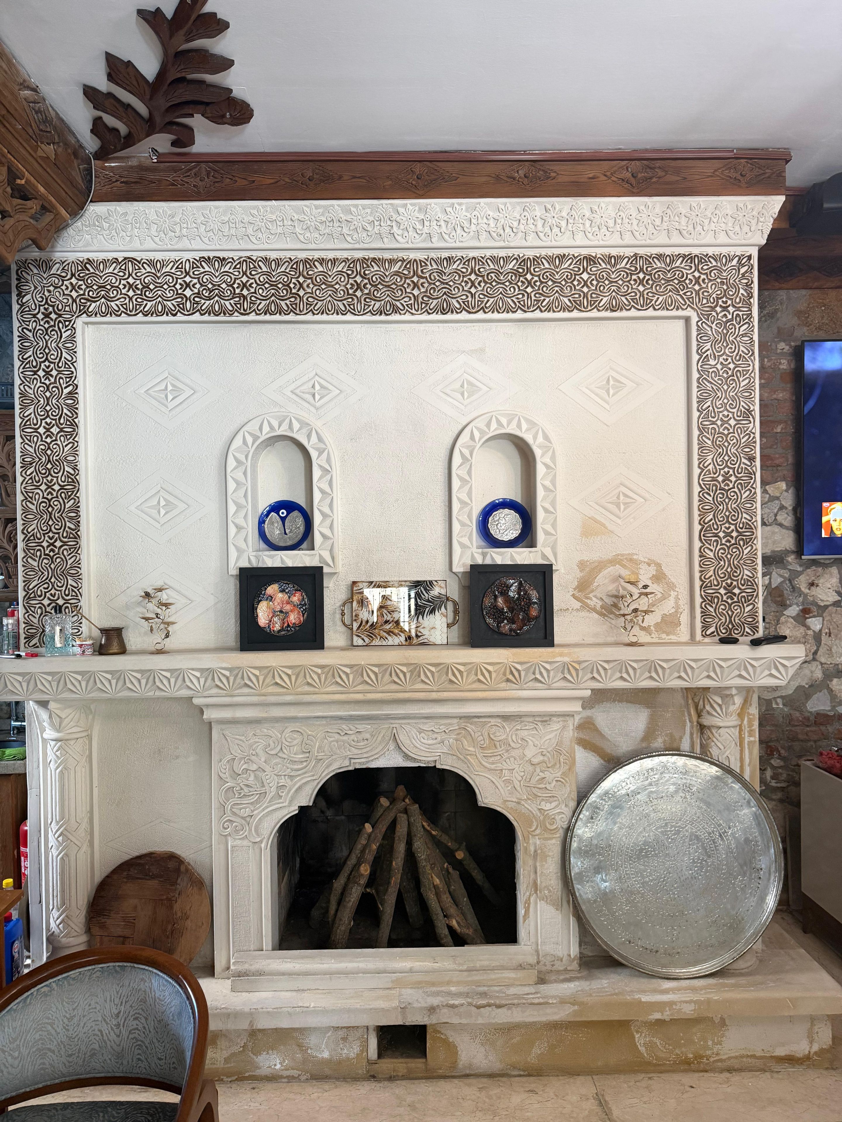 Una chimenea con elaborados diseños blancos y marrones, un repisa con obras de arte enmarcadas y una pared de piedra.