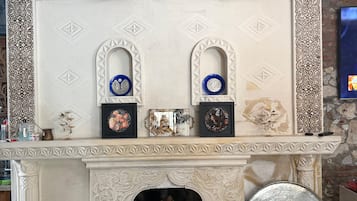 Una chimenea con elaborados diseños blancos y marrones, un repisa con obras de arte enmarcadas y una pared de piedra.