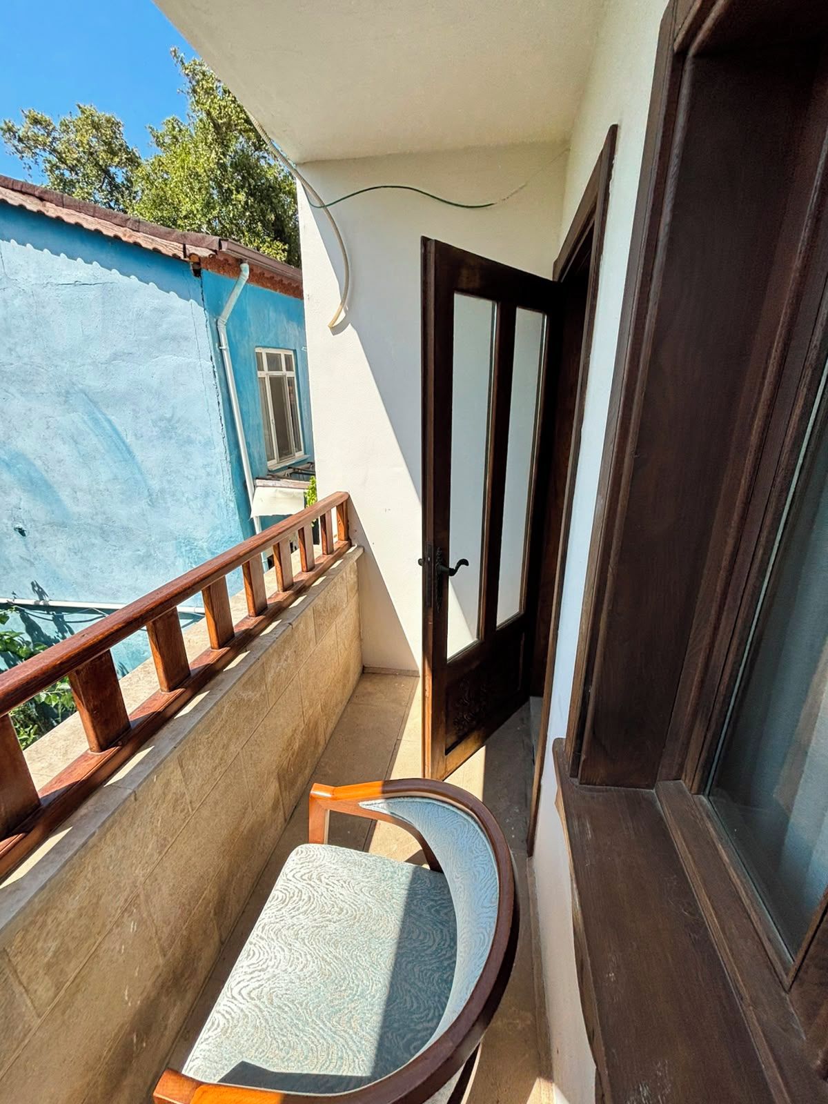 Un balcon étroit doté d’une balustrade en bois, d’une petite table et d’une porte donnant sur un espace intérieur.