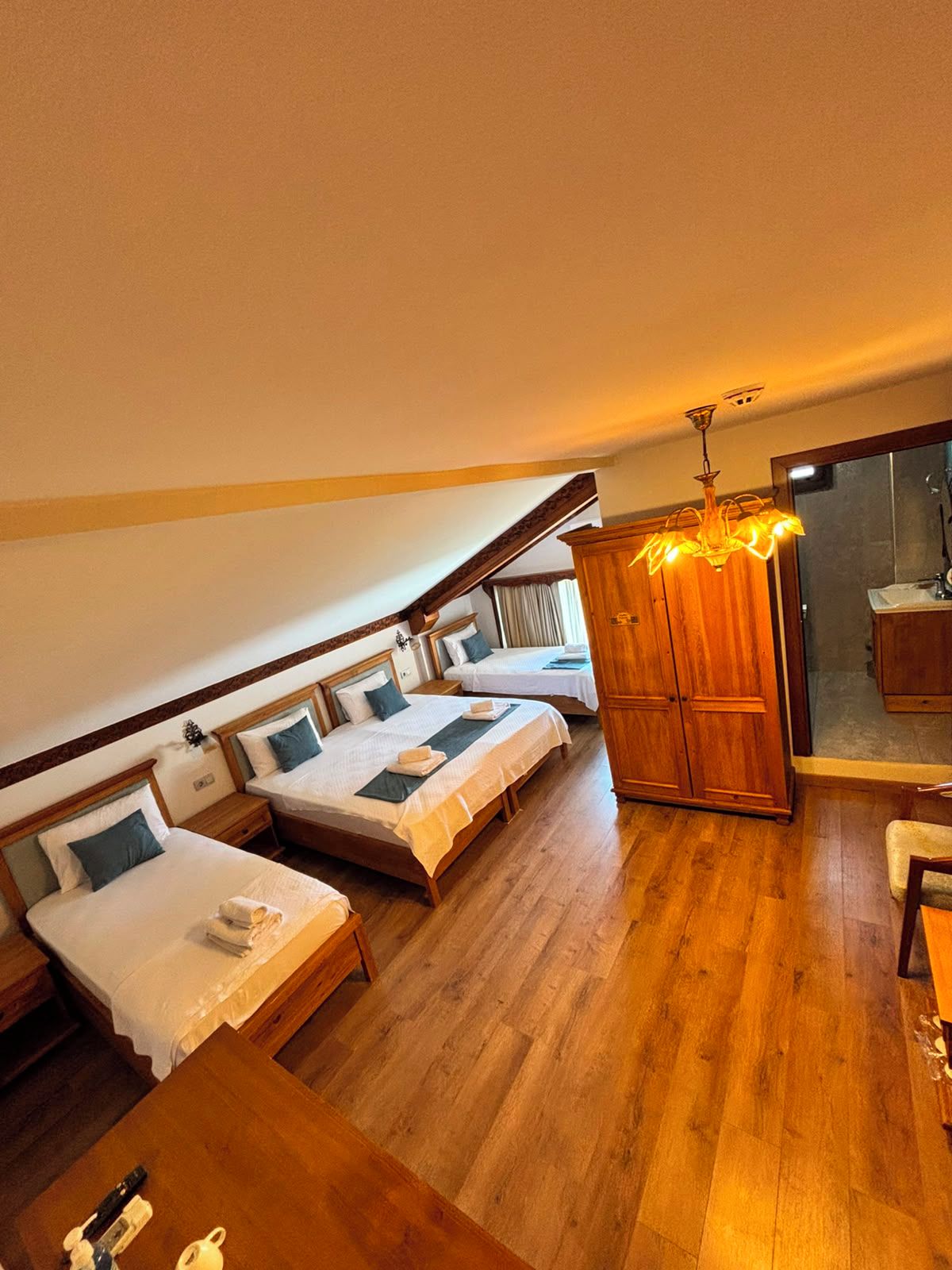 A hotel room with two beds, a wooden wardrobe, a dining table, and a chandelier.