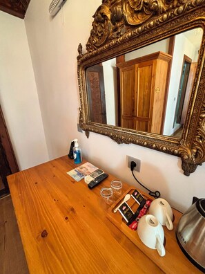 Una mesa de madera con un espejo, un teléfono, una caja de pañuelos, una botella de desinfectante de manos y un hervidor.