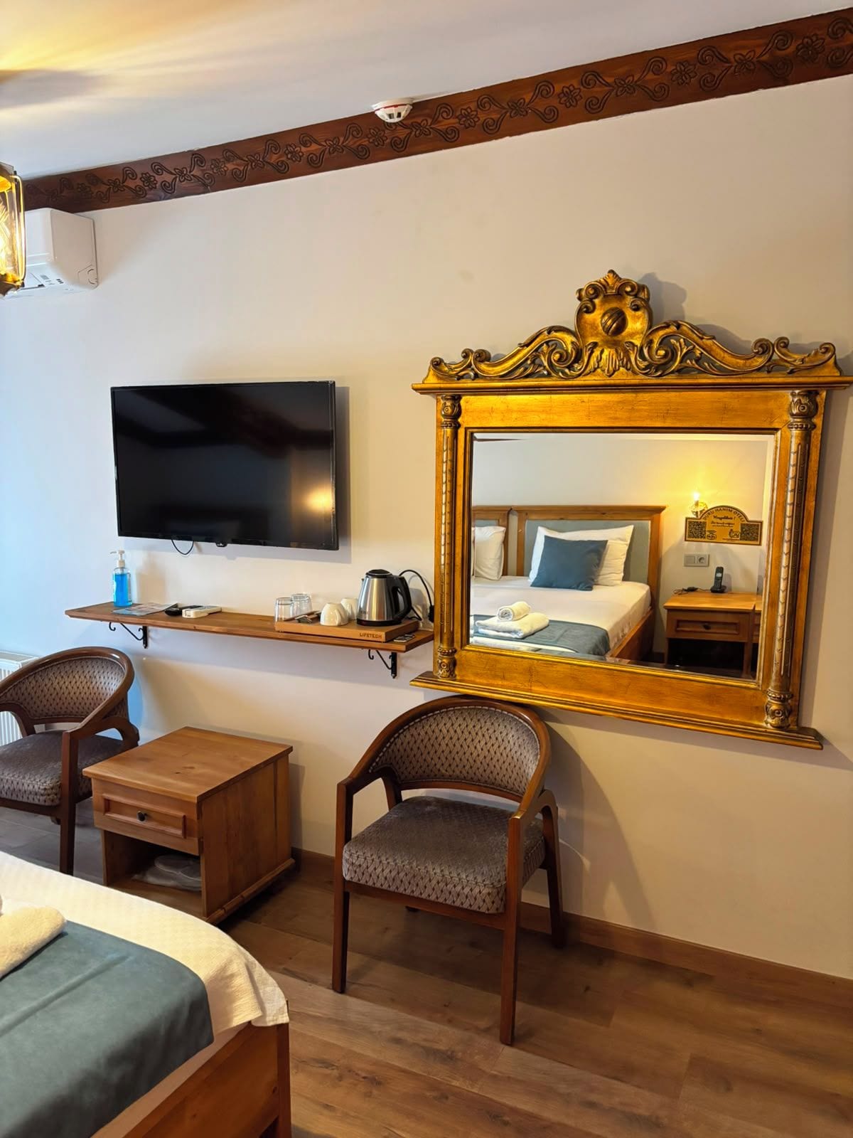 A hotel room with a bed, a television, a mirror, a desk, and two chairs.