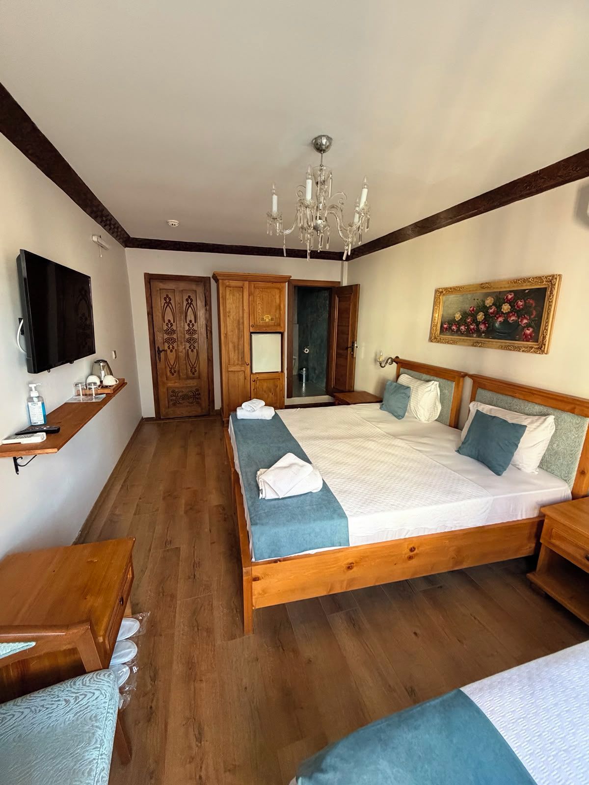 Un dormitorio con una cama de madera, un televisor, una araña y un cuadro en la pared.