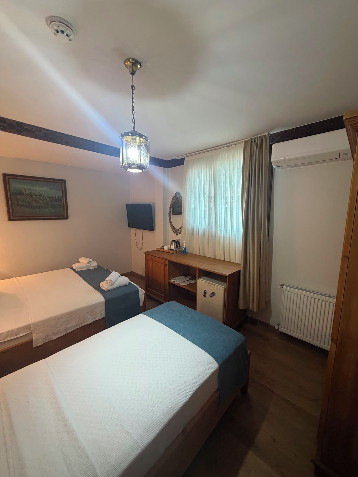 Habitación de hotel con dos camas individuales, un escritorio de madera, un espejo, un televisor y un radiador.