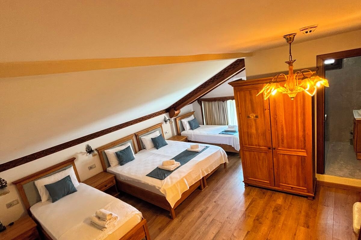 A hotel room with two single beds, a wooden table with a bottle and glasses, and a chandelier.