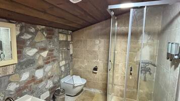 Un baño con pared de piedra, lavamanos blanco, inodoro y ducha con cerramiento de vidrio.