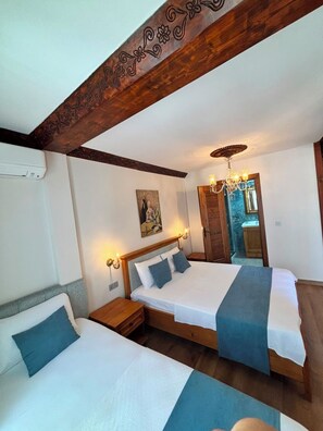A bedroom with two beds, a wooden ceiling beam, a chandelier, and a painting on the wall.