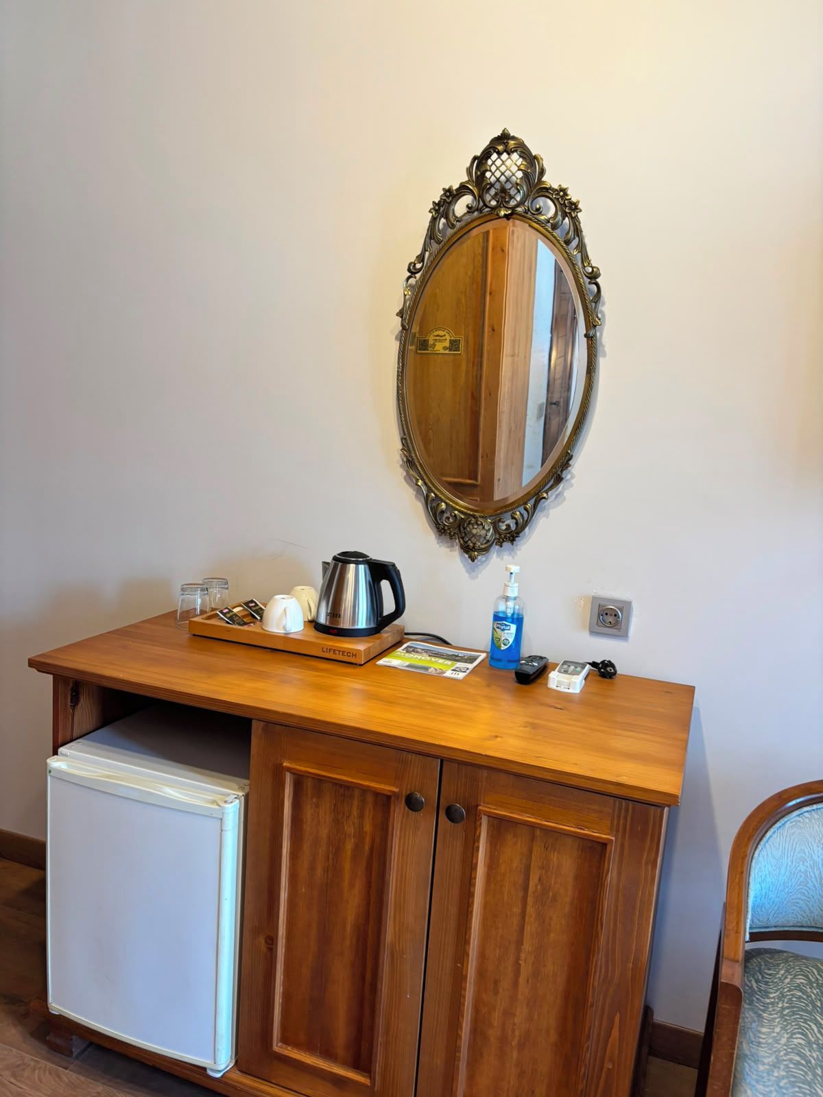 Una scrivania in legno con uno specchio, un bollitore, una bottiglia di sapone per le mani e un telecomando.