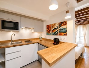 A modern kitchen with a microwave, sink, and wooden countertop. There is a coffee maker on the counter and a potted plant. The room has white cabinets and a wooden ceiling. - 1619 Colombier (Paris)