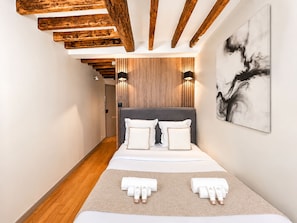 A modern hotel room with a wooden ceiling, a large bed with white bedding, two bedside lamps, and a wall-mounted abstract painting. - 1619 Colombier (Paris)