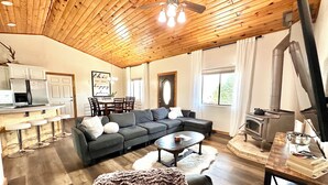 A cozy living room with a wooden ceiling, a sectional sofa, a coffee table, and a fireplace. - The Sunflower Cabin - Pets, Continuous hot water, Traeger grill, Starlink, AC (Overgaard)