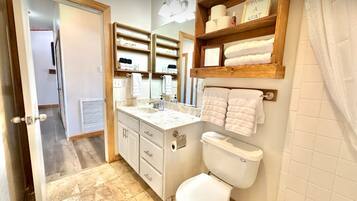 A bathroom with a toilet, sink, and vanity, featuring a wooden shelf with towels and toiletries.
