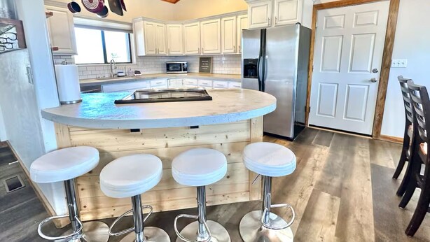 A modern kitchen with white cabinets, a stainless steel refrigerator, and a central island with bar stools. - The Sunflower Cabin - Pets, Continuous hot water, Traeger grill, Starlink, AC (Overgaard)