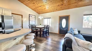 A modern kitchen with a wooden ceiling, a dining area with a chandelier, and a cozy living space with a sofa. - The Sunflower Cabin - Pets, Continuous hot water, Traeger grill, Starlink, AC (Overgaard)