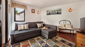 Ein modernes Wohnzimmer mit einem grauen Ecksofa, einem gemusterten Teppich, einer Holzbank und einem Fernseher auf einem Holzboden.