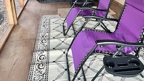 A covered patio area with a hot tub, two purple lounge chairs, and a patterned rug. - UPSCALE EAST TEXAS CABIN, PRIVATE HOT TUB, WIFI, ROKU, OLD MILL VILLAGE KENNARD (Kennard)
