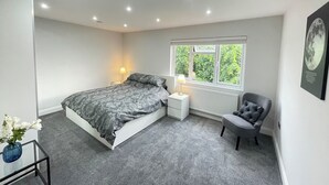 Une chambre moderne avec un lit, une table de chevet, une chaise et une fenêtre donnant sur un paysage verdoyant.