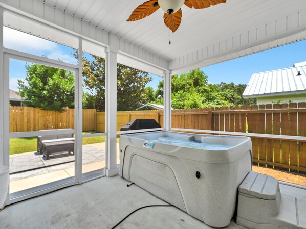 A covered outdoor area with a hot tub, a wooden bench, and a patio table.