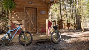 Una pequeña cabaña de madera con un letrero que dice "WILDERNESS RESORT" y un cartel con la leyenda "HAPPY TRAILS" sobre la puerta. Hay dos bicicletas estacionadas al frente.