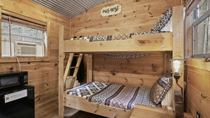Habitación tipo cabaña de madera con literas, una escalera, un escritorio con computadora y una ventana con persianas.