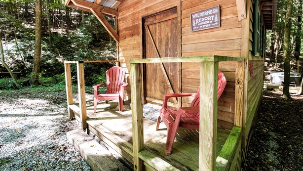 Una cabaña de madera con un porche, dos sillas Adirondack rojas y un letrero que dice 'Wilderness Resort'.