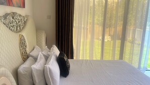 Una camera d'albergo con un letto, cuscini, una testiera, una finestra con tende e un quadro appeso al muro.
