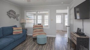 Una sala de estar con un sofá azul, un sillón a rayas y un reposapiés, una lámpara y un televisor sobre un mueble de madera.