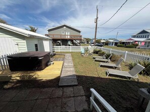 Ein Garten mit Whirlpool, einer Holzterrasse und einem eingezäunten Bereich mit Liegestühlen.