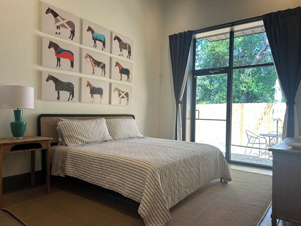 Un dormitorio con una cama grande, una mesita de noche con lámpara, una pared decorada con motivos ecuestres y una ventana con cortinas.