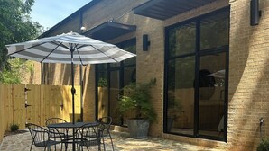 Une terrasse avec un sol en pierre, une table avec des chaises et un grand parasol.