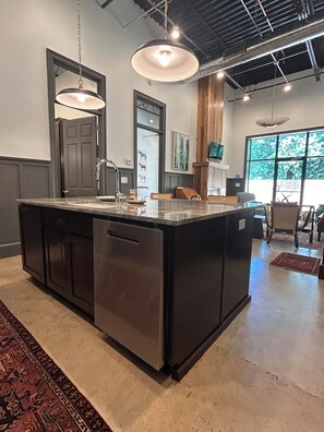 Una cocina moderna con una isla grande, electrodomésticos de acero inoxidable, iluminación colgante y vistas al exterior a través de amplios ventanales.