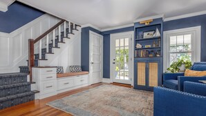 A spacious living room with a wooden staircase, a blue sofa, and a bookshelf. - Beautiful 3-bedroom house in New Paltz with AC, WiFi, SunDeck & Close to ALL (New Paltz)