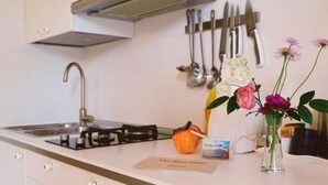 Una cocina con estufa a gas, un fregadero y un soporte para cuchillos. Hay flores en un jarrón y una pequeña calabaza en la encimera.