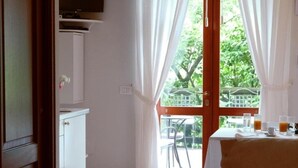 Una habitación con una cama, una mesa con alimentos para el desayuno, una ventana con cortinas y vistas a zonas verdes.
