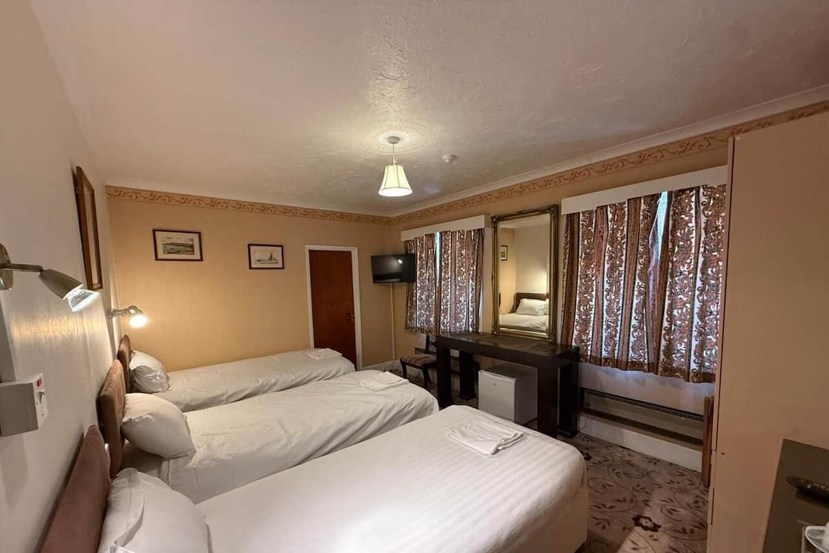 A hotel room with two beds, a desk, a television, and a mirror.