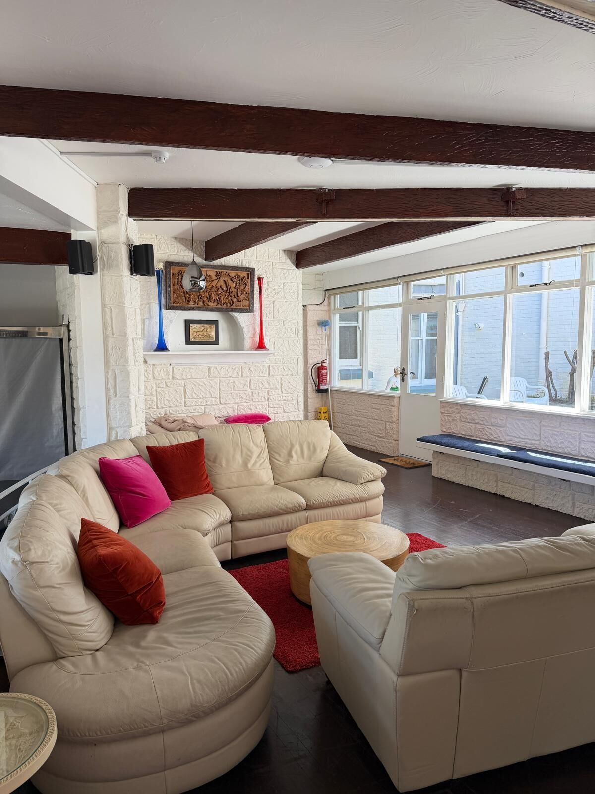 Een woonkamer met een hoekbank, een ronde salontafel en een bankje bij een groot raam.