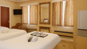 A hotel room with two beds, a desk, a chair, a TV, and a tray with towels and a remote control. - The Queens Road Hotel (Shanklin)
