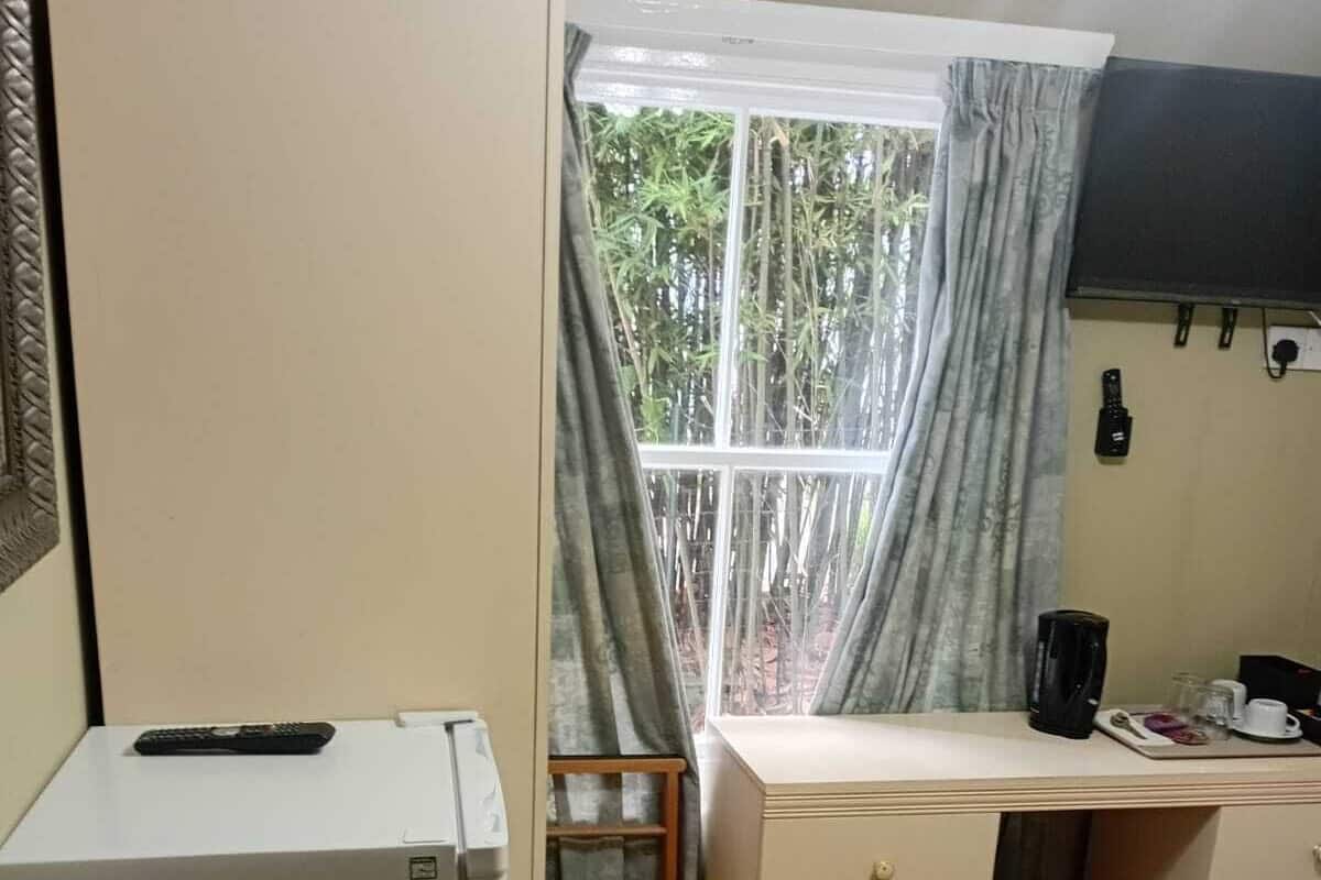 A compact hotel room with a bed, a desk with a chair, a refrigerator, and a window with curtains.