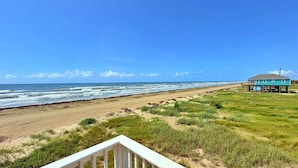 A beach house with a deck, ocean view, and grassy area.