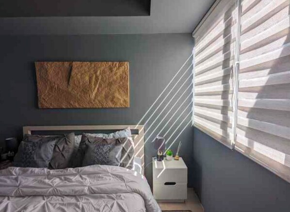 Ein Schlafzimmer mit einem Bett, einem Nachttisch, einem Wandbild und einem Fenster mit Jalousien.