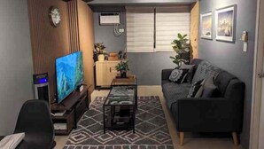 A modern living room with a flat-screen TV, a sofa, a coffee table, and a decorative plant. - NYC Vibes! 1-BR Condo in BGC with Pool, AC, Hi-Speed WiFi, Netflix! Sleeps 2-3 (Taguig City)