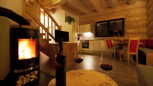 A cozy living room with a wood-burning stove, a bottle of wine, and two glasses on a wooden table. - Cosy Chalet with Panoramic View, Sun Terrace and Free Summer Mountain Cable Car (Ladis)