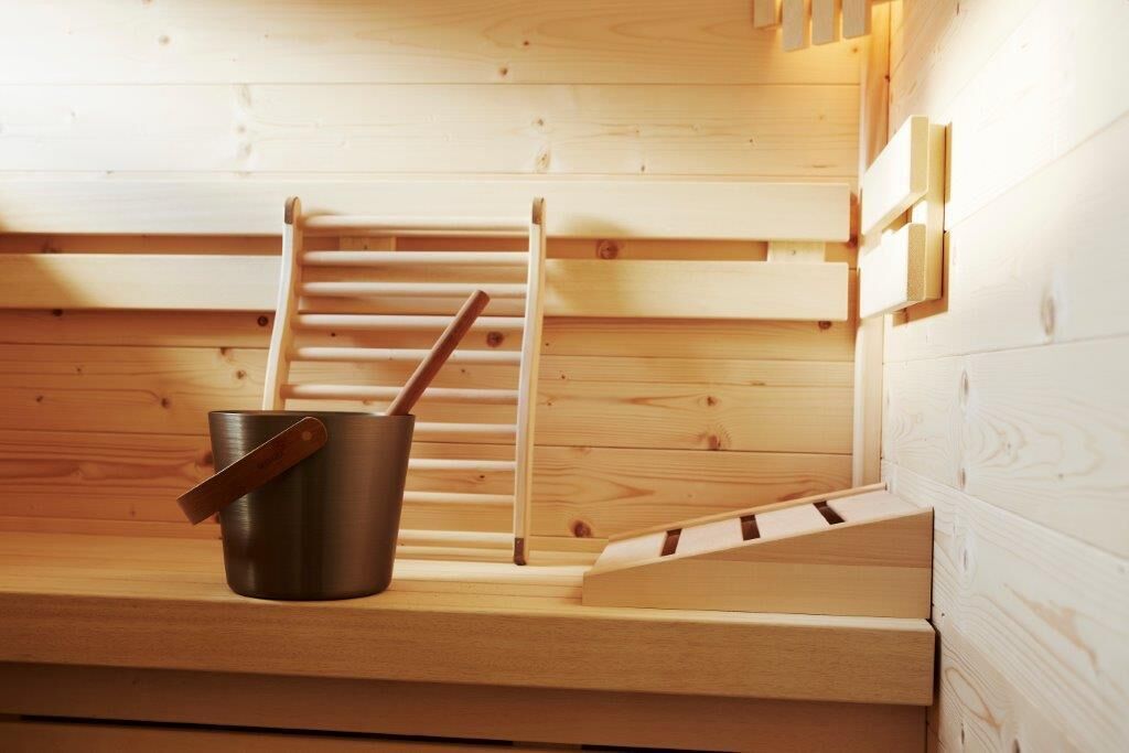 Uma sauna com um banco de madeira, um balde de metal e um porta-toalhas de madeira.